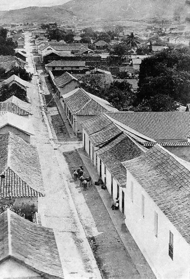 Calle de la Cárcel. 1874 Esquina suroeste de la plaza principal. A la derecha se observa la Casa Municipal, donde también quedaba la cárcel. En el centro de la calle se construían acequias que conducían las aguas lluvias. Fuente: Cámara de Comercio de Cúcuta