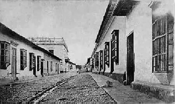 Calle del Comercio.1874. Esta era una calle típica de Cúcuta antes del terremoto con una acequia en el centro y empedrado en toda la calle. Las casas tenían ventanas y portones amplios y algunas casas eran de 2 pisos con azotea, como la del fondo a la izquierda que pertenecía a Juan Aranguren y era la mas suntuosa de la ciudad. Fuentes: Cámara de Comercio de Cúcuta y el doctor Virgilio Durán Martínez.