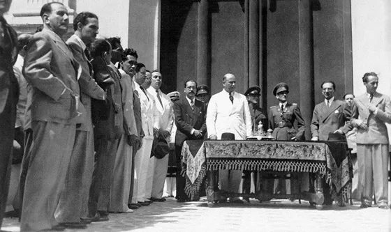 Visita del Presidente de Venezuela Isaías Medina. Están ubicacados frente a la puerta principal de la Catedral de San José. De izquierda a derecha de la mesa aparecen, de traje oscuro Carlos Ardila Ordóñez, Gobernador del Departamento; de traje blanco Isaías Medina, Señor Presidente de Venezuela; y con las manos en los bolsillos Gabriel Turbay, Ministro de Relaciones Exteriores de Colombia. Los acompañan autoridades militares de los 2 paises y personalidades de la ciudad. Julio 18 de 1943.