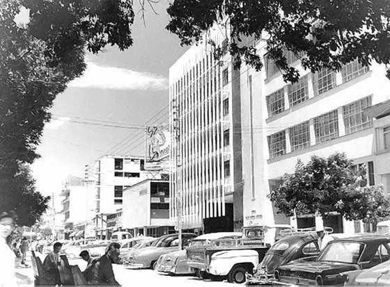 Avenida 6a entre Calles 10 y 11. Se alcanza a apreciar la publicidad de Cigarrillos Piel roja que fue una de las marcas mas populares de nuestro país, también se observa el Banco Bogotá y el Banco Comercial Antioqueño y al fondo parte de la edificación de Las Empresas Municipales. Década de los 70.