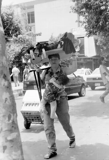 Vendedora informal se dirige con su hijo a colocar su puesto de venta en el centro de la ciudad. foto década del 90.